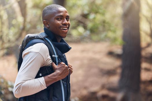 One young handsome african american male backpacker hiking outdoors in the woods. Confident and happy black man walking through the forest, sightseeing and enjoying his favourite weekend activity
