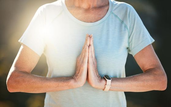 Close up of a senior woman standing outside with joined hands in namaste position, meditating in nature. Finding inner peace, balance and living healthy