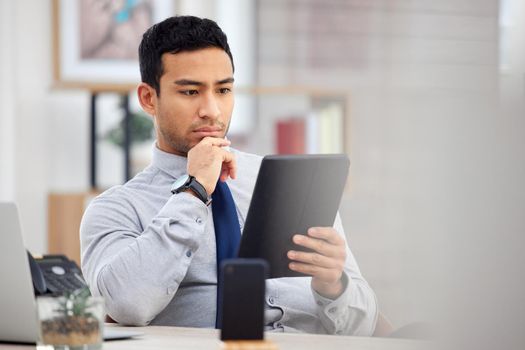 Mixed race businessman holding and using a digital tablet sitting in an office at work. One focused hispanic male businessperson using social media on a digital tablet at work