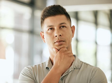 Thoughtful mixed race young business man with hand on chin planning project, pondering ideas. Pensive professional thinking about future while standing in an office