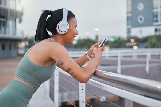 Sporty young african american woman texting while exercising outside. Mixed race female athlete using a cellphone in the city. Checking social media while taking a break to enjoy music with headphones