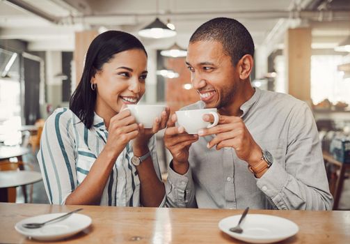 Loving mixed race couple in love looking at each other while holding cups enjoying coffee in a cafe. Happy young woman and man on their first date in a restaurant