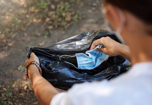 Closeup of a woman throwing a mask in a trash bag. Community cleanup project. Cleaning the planet and collecting trash. The end of a global pandemic leaves a mess. Female doing community service.