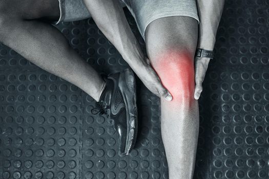 Joint ache is common in the gym. Trainer touching their knee in pain from above. The knee joint is prone to injury. Closeup of athlete in pain at the gym. CGI red spot of pain on trainers knee