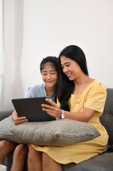 Asian mom and daughter having fun browsing internet on digital tablet together on sofa
