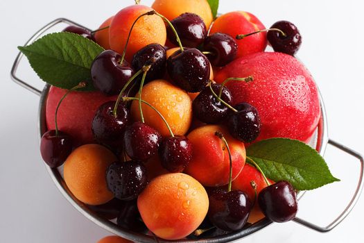 apricots and cherries in a metal bowl on a white background. Close-up