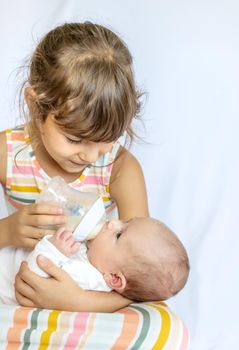 An older sister is feeding a newborn baby. Selective focus.