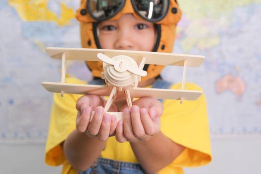 Little girl in a pilot hat holding a toy plane in her hands having fun in kids room at home. Happy child girl at home dreaming of travel and tourism. Childhood dream imagination and Travel concepts.