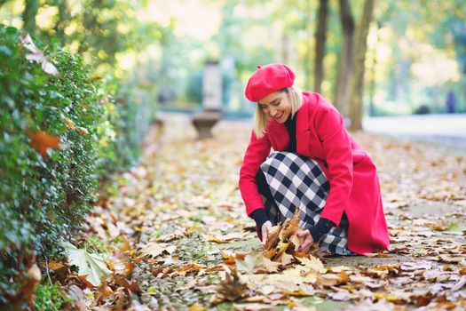 Smiling woman collecting leaves from ground in park