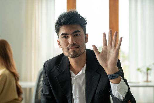 Webcam portrait of asian businessman looking directly at camera with friendly smile, waving hand, greeting gesture