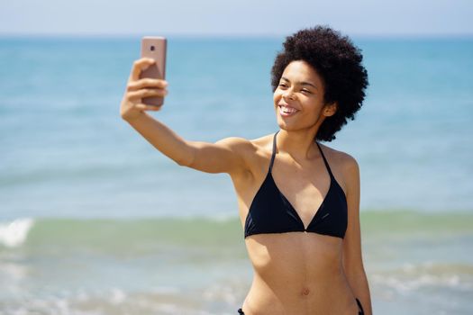 Black woman in bikini taking selfie near sea