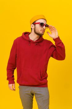 Young pensive handsome caucasian man in Great Britain flag sunglasses and casual wear, looking away isolated on yellow background. Stylish bearded smart hipster man casual look