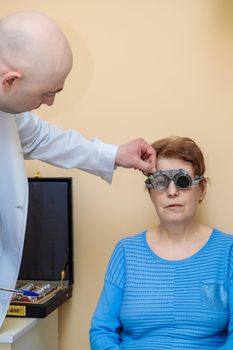 A male optometrist checks the eyesight of an adult woman with a trial frame