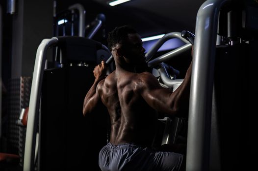 Shirtless african american man doing back exercises on a machine in the gym.