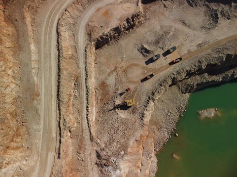 Aerial view of industrial opencast mining quarry with lots of machinery at work - extracting fluxes for the metal industry. Oval mining industrial crater, acid mine drainage in rock.