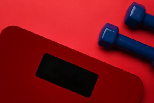 Digital scales and dumbbells on red background. Loosing weight and healthy lifestyle concept.