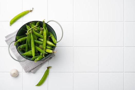 Raw Green Organic Snow Peas on white ceramic squared tile table background, top view flat lay, with copy space for text
