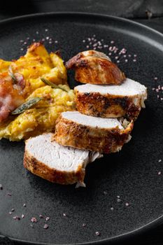 Roasted pork loin with mash potatoe gratin, sage and prosciutto, on plate dish, on black wooden table background