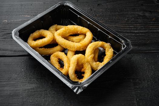 Heap of deep fried squid or onion rings package, on black wooden table background, with copy space for text