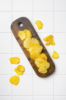 Wavy Potato Chips on white ceramic squared tile table background, top view flat lay