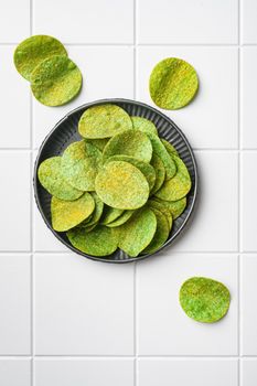 Green potato chips on white ceramic squared tile table background, top view flat lay, with copy space for text
