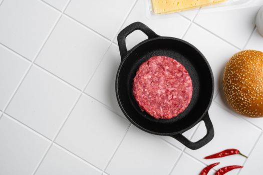 Raw fresh large beef burger on white ceramic squared tile table background, top view flat lay, with copy space for text