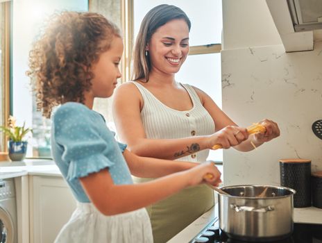 Mother and little daughter cooking together in the kitchen. Mixed race mother and child standing by the stove breaking spaghetti and throwing it in boiling water