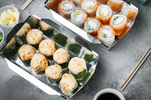 Tasty sushi rolls in disposable boxes, on gray stone background