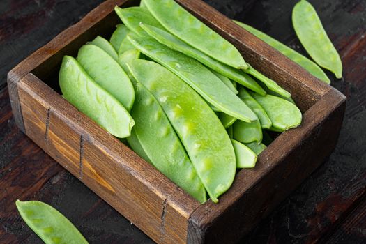 Fresh organic mangetout, also known as sugar snap pea, in wooden box, on old dark wooden table background