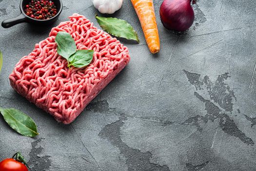 Ingredients for cooking Bolognese sauce, minced beef meat tomatoe and herbs, on gray stone background, with copy space for text