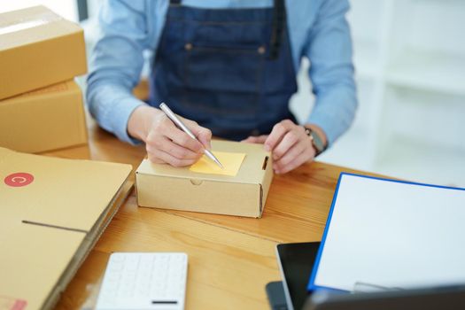 small startup, and SME owner, an Asian male entrepreneur, is writing down information on a notepad to organize the product before packing it into the inner box for the customer