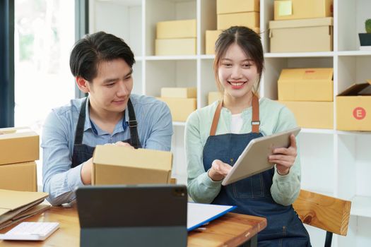 Portrait of a small start-up and SME owner, an Asian male and female entrepreneur checking orders and packing for customers, self-employed, freelance, online selling