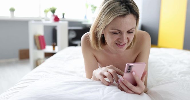A woman after a shower lies on a bed with a phone