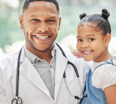 Portrait of handsome young black paediatrician holding adorable little girl in hands, cute child and doctor smiling during medical check up in clinic