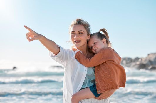 Mother and daughter on vacation by the sea. Child enjoying a getaway with her caucasian mom on a bright summer day, smiling family relaxed against a bright copyspace background while pointing