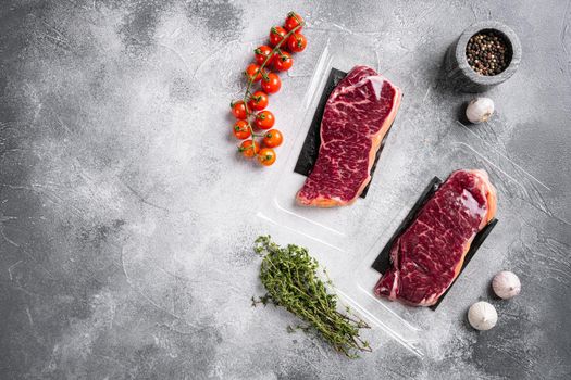 Raw marbled beef steaks in vacuum pack, on gray stone table background, top view flat lay, with copy space for text