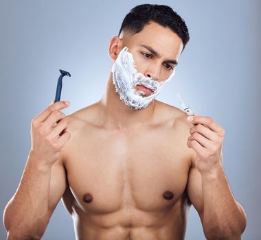 Opinions differ vastly on them. Shot of a young man unable to decide between razors against a studio background.