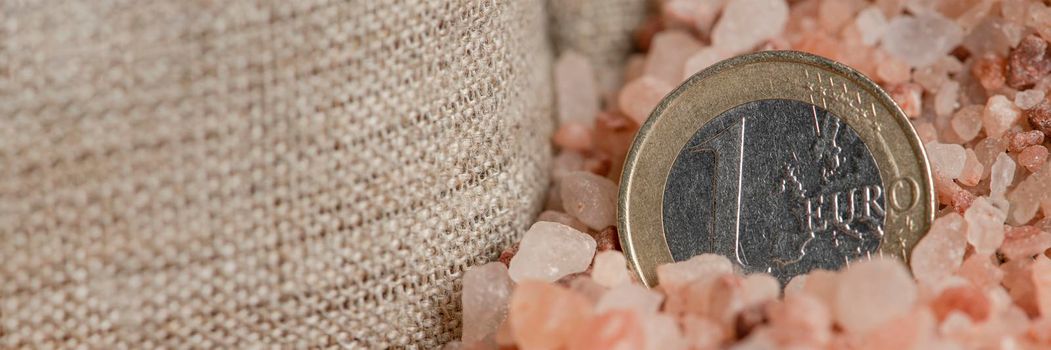 Salt price. Large crystals of pink Himalayan salt, close-up. A coin in a pile of salt as a symbol of rising prices.