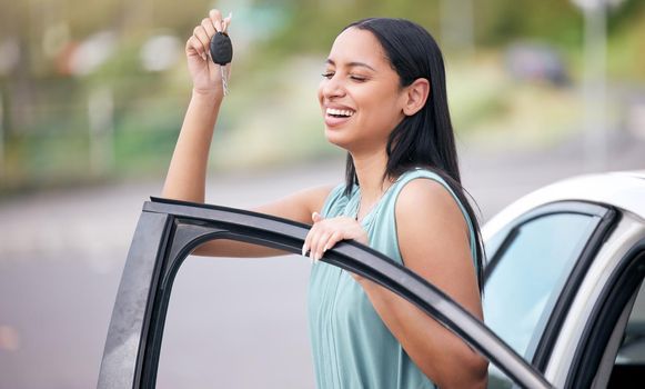 A cheerful mixed race woman holding keys to her new car. Hispanic woman looking happy buying her first car or passing her drivers test. Hispanic woman smiling against bright copyspace