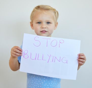 Little girl protesting against bullying with a sign. Adorable caucasian child standing alone and holding a protest poster against white background. Kid campaigning against bullying