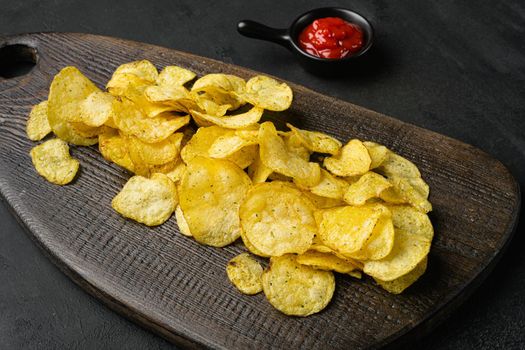 Crispy potato chips on black dark stone table background