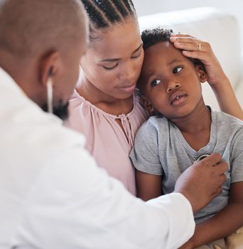 African american male paediatrician examining sick boy with stethoscope during visit with mom. Doctor checking heart lungs during checkup in hospital. Sick or sad boy receiving medical care