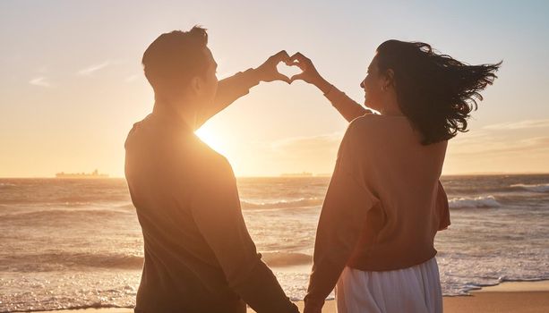 Biracial couple holding their hands together in a heart shape at the beach. Biracial couple holding their hands together in a heart shape at the beach.