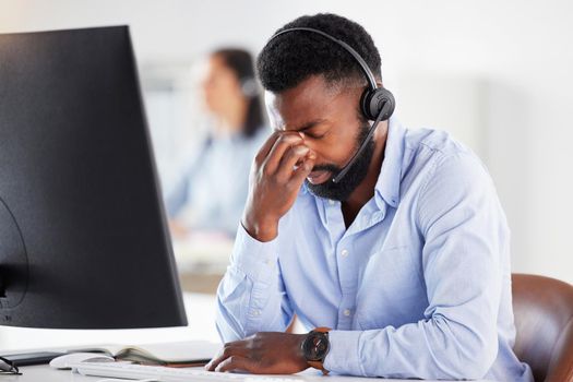 One stressed young african american male call centre agent getting a headache while working on computer in office. Consultant making mistakes and struggling with difficult customers when operating a support helpdesk