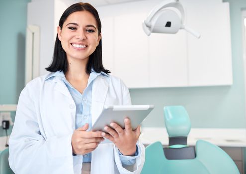Young female caucasian dentist wearing a labcoat and smiling while using a digital tablet in her office. Dental hygiene is important to your wellbeing