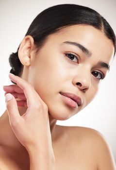 Young beautiful mixed race woman touching and feeling her face posing against a grey studio background. Confident hispanic female posing against a background