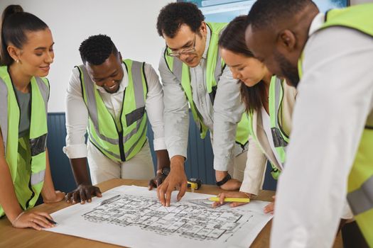 Closeup of a happy diverse multiracial group of architect colleagues analyzing a blueprint design on a building and discussing plans for the next project. Team of young and senior designers working on a strategy for a building construction plan while wearing reflectors