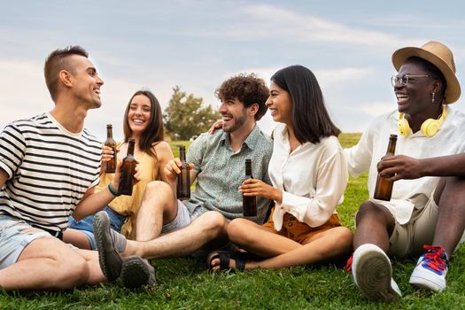 Multiracial friends laughing together enjoying some cool beer outdoors in park. Having fun.