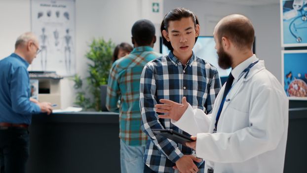 General practitioner talking to asian man about diagnosis on digital tablet