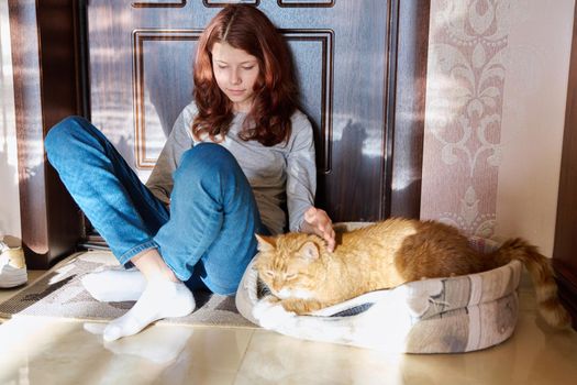 Preteen girl sitting on floor at home using smartphone, with sleeping pet cat